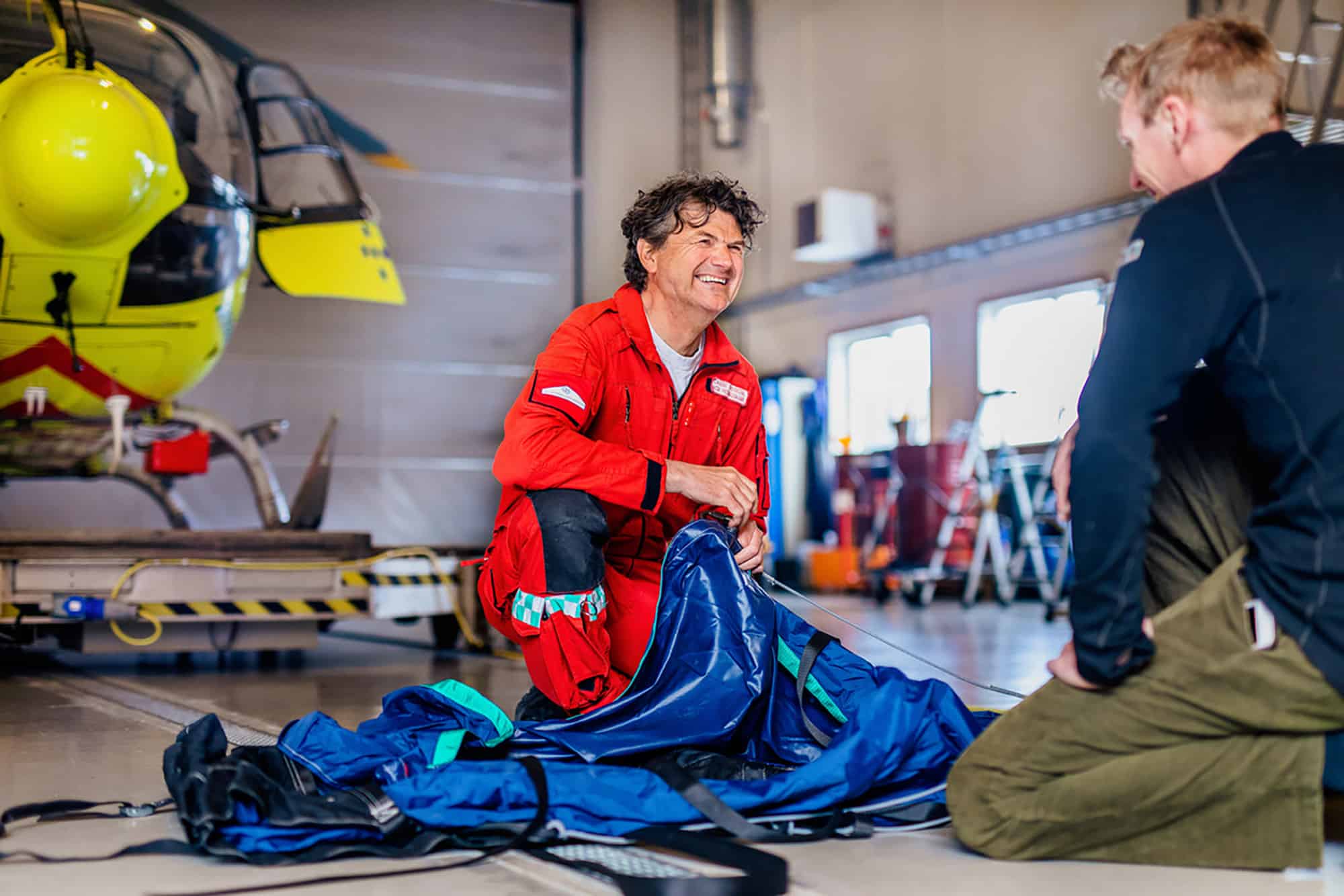 Redningsmann Lasse Fossedal pakker utstyr og snakker med en kollega foran legehelikopteret inne i hangaren