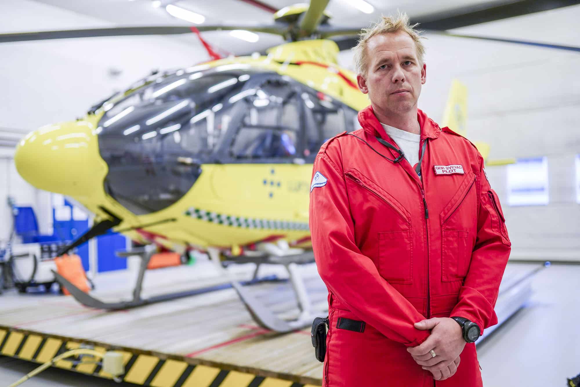 Pilot Geir Svevad i hangarden med helikoptret bak seg. Foto VG Partnerstudio