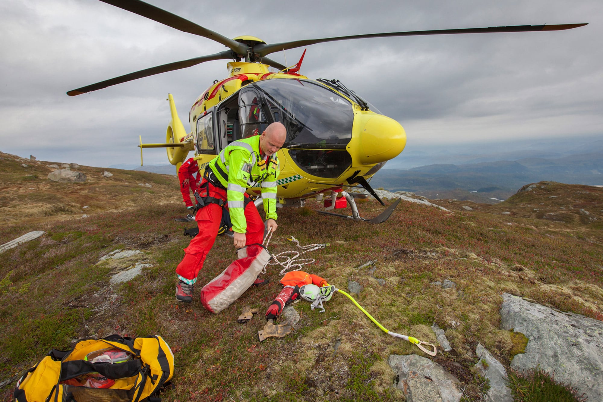 Redningsmann gjør klart utstyr foran legehelikopteret, som har landet på en fjelltppp