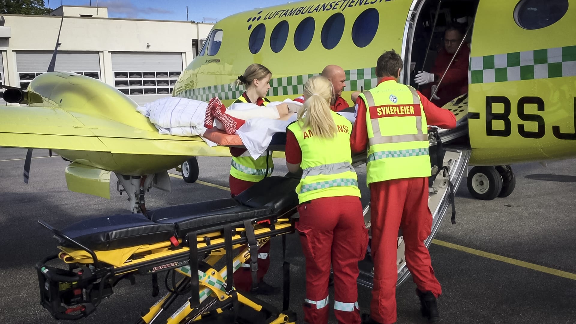 Ambulansearbeider og sykepleier løfter pasient inn i fly