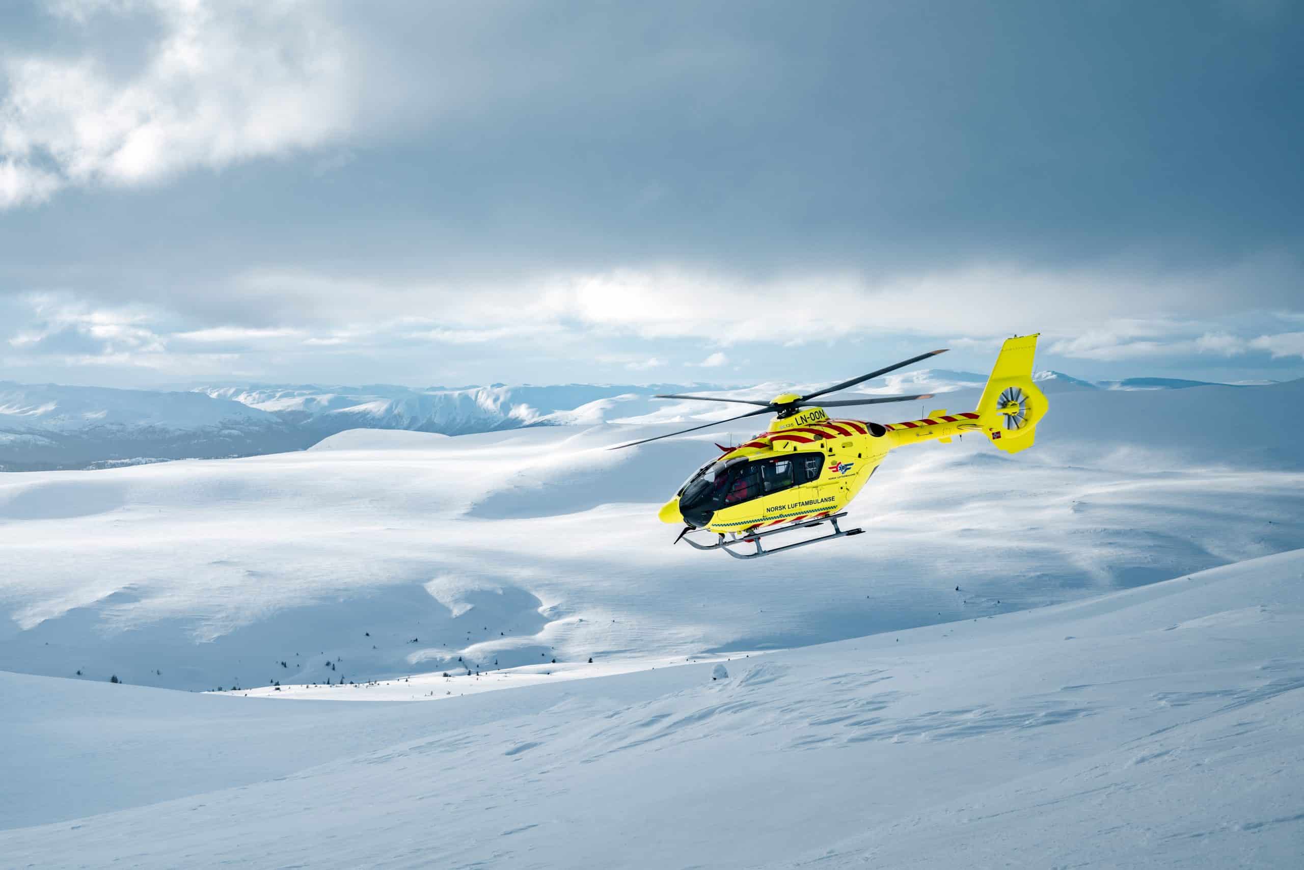 Gult legehelikopter flyr over snølandskap
