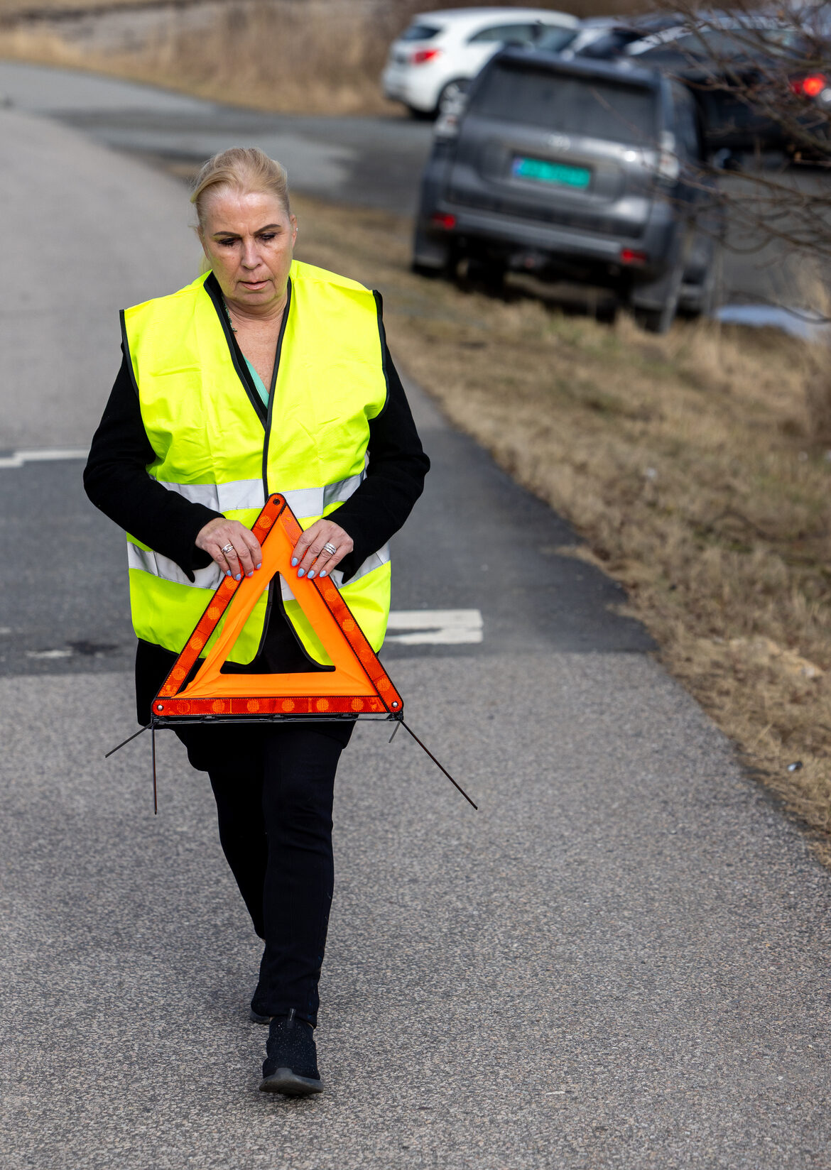 Kvinne går på veien med varseltrekant. 