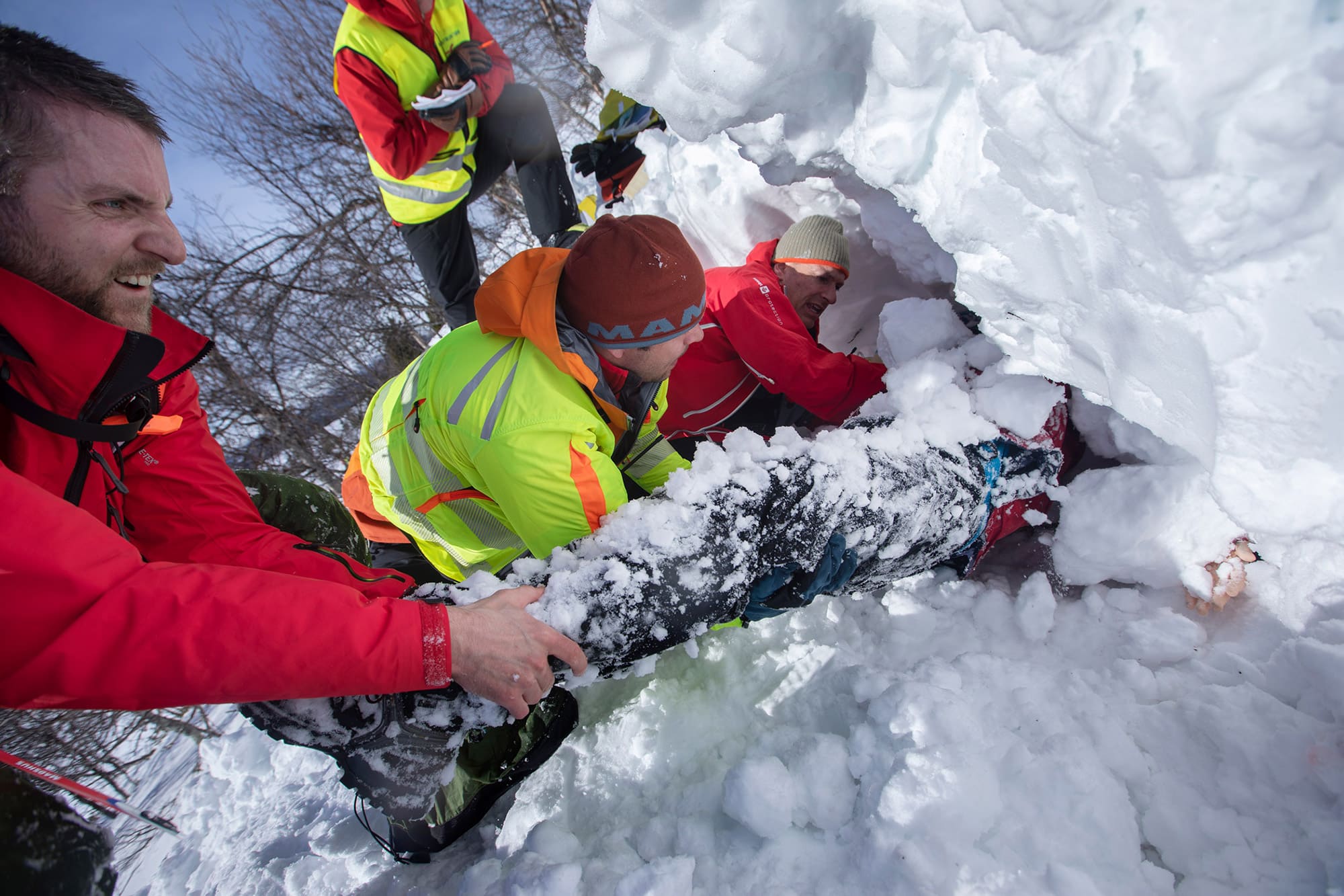 Luftambulansepersonell graver etter pasient under snøen under øvelse. De har gravd frem ett bein.