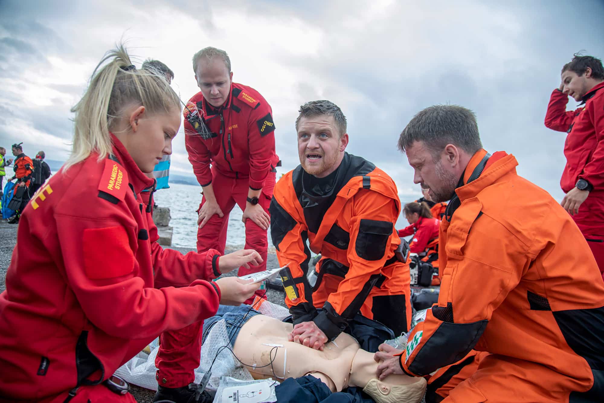 Redningsdykker og ambulansepersonell øver på hjerte- og lungeredning på dukke ved vannet.