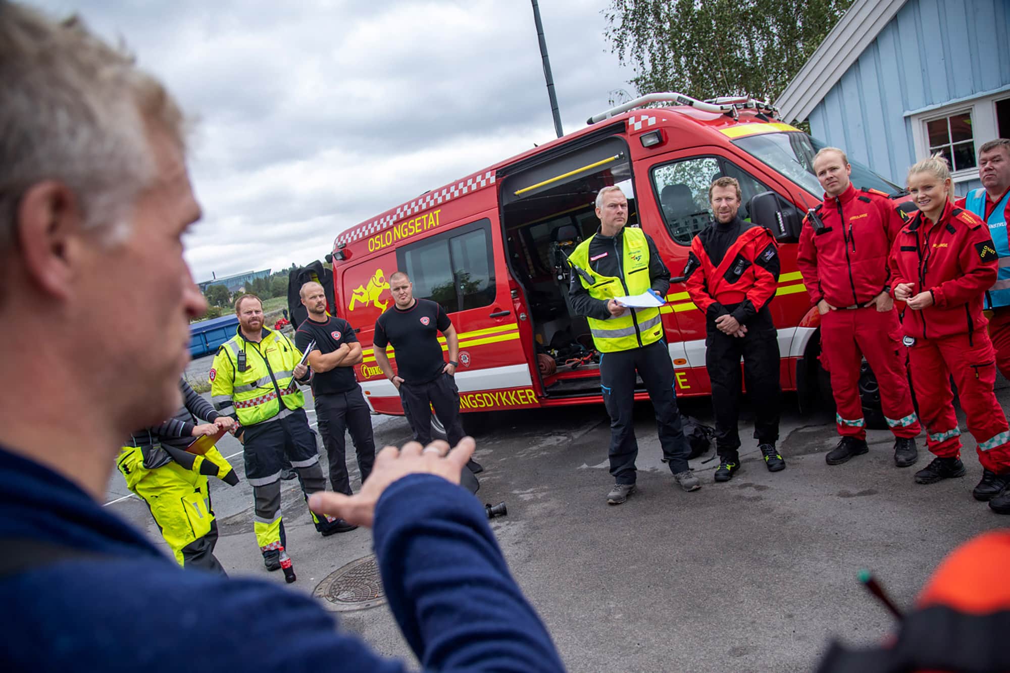 Debrief etter øvelse, redningsmannskaper fra ulike yrkesgrupper står i sirkel foran brannbil.