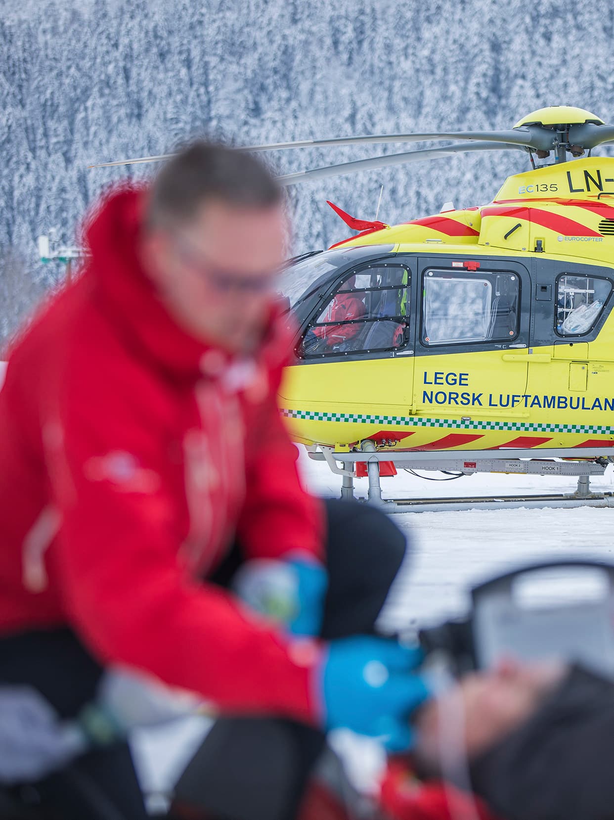 Luftambulanselege jobber med pasient på øvelse, legehelikopteret i bakgrunnen.