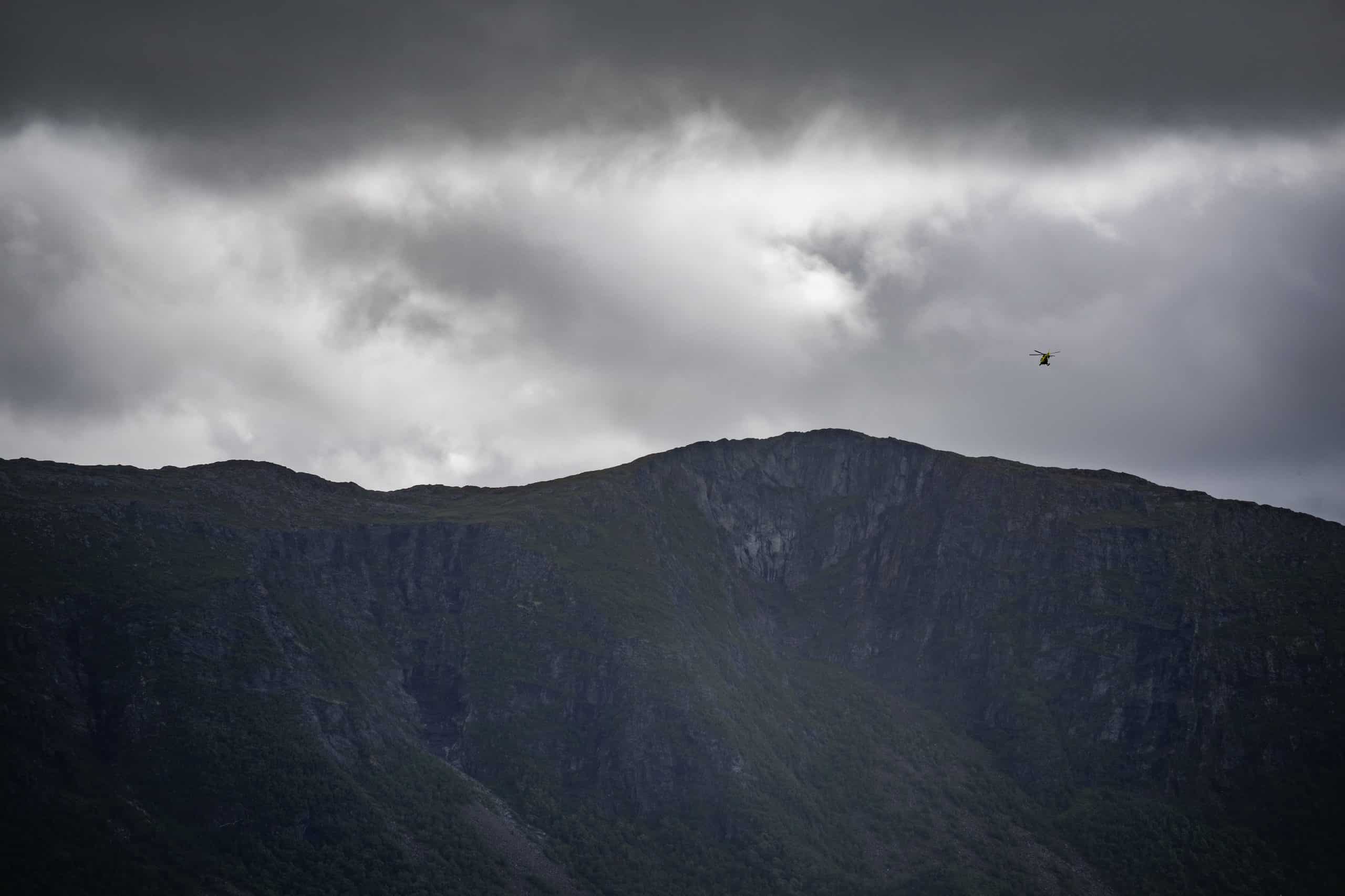 Helikopter flyr over fjell i skyete vær