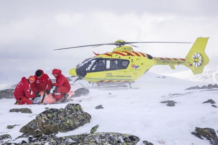 Gult legehelikopter i vinterlandskap. Mannskapene hjelper en skadelidende person. Forskning bidrar til å styrke luftambulansetjenesten i Norge.
