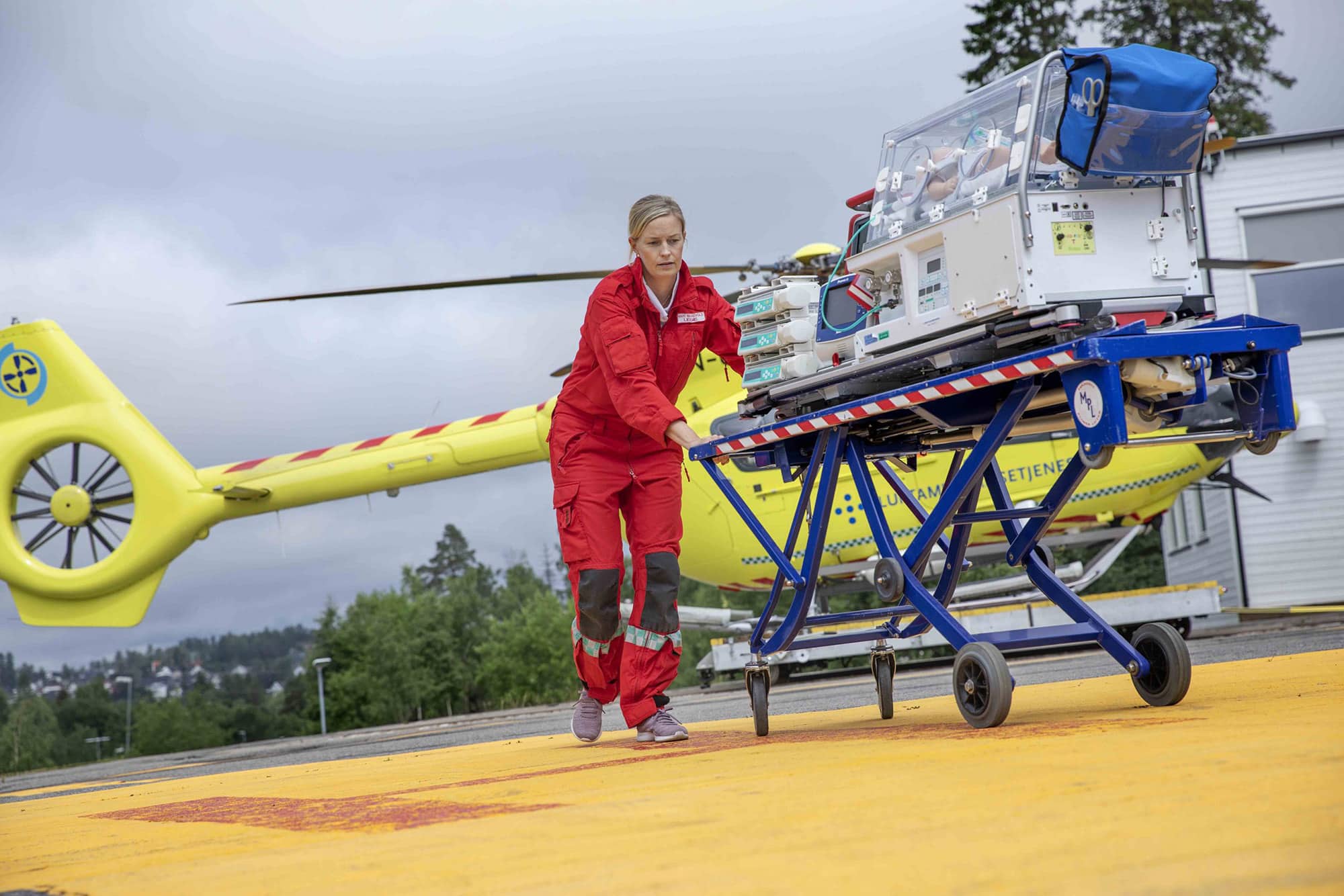 Luftambulanselege Marit Bekkevold triller en barnekuvøse på båre over helikopterlandingsplassen.