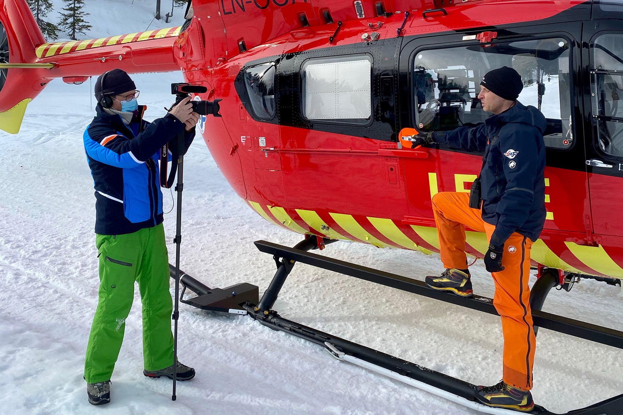 Kameramann filmer lege i Norsk Luftambulanse utenfor helikopter på snøen.