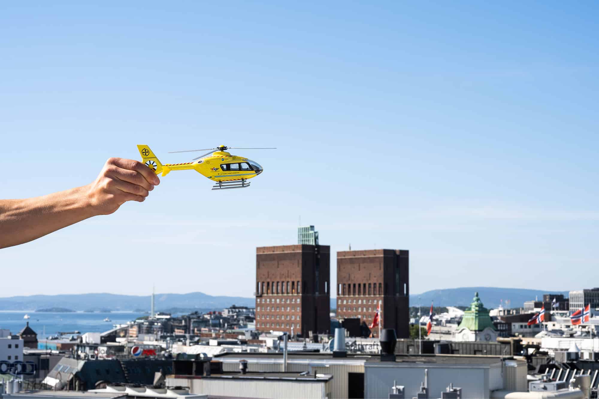 Bilde av Rådhuset i Oslo en sommerdag, illustrert med en hånd som holder et helikopter over.