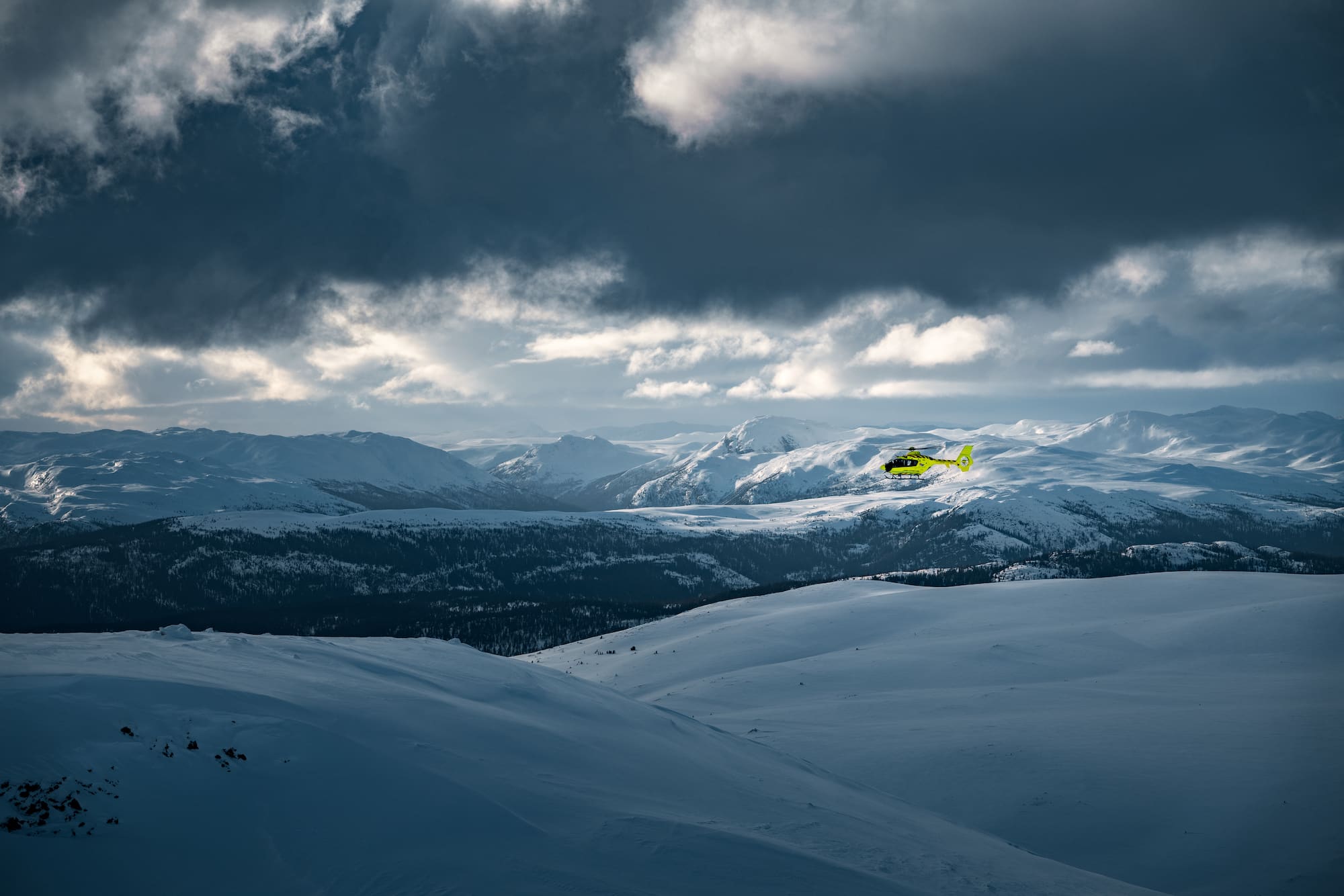 Luftambulansehelikopter flyr i vinterlandskap på fjellet