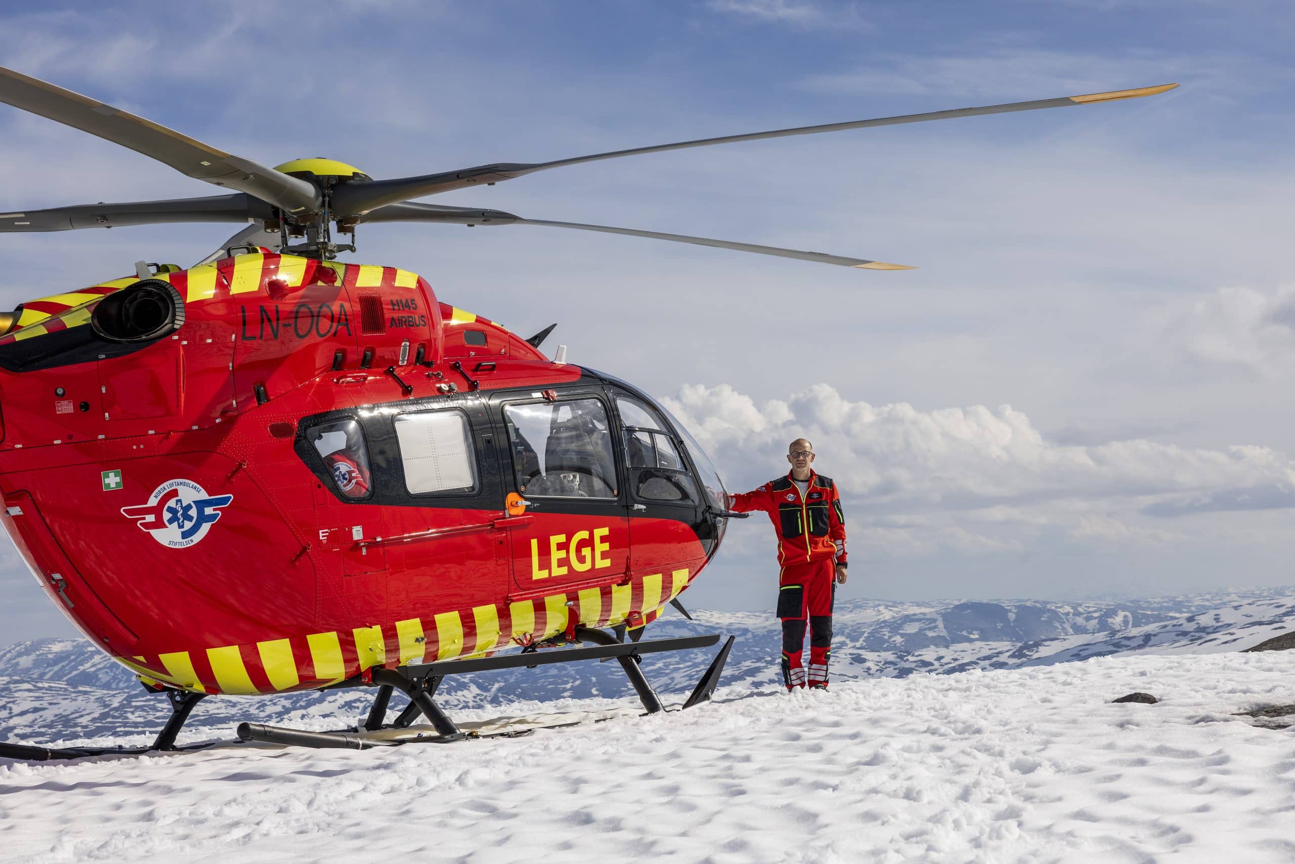 Pilot Erik Normann og luftambulansens utviklingshelikopter fotografert på en fjelltopp mellom Majavatn og Brønnøysund.