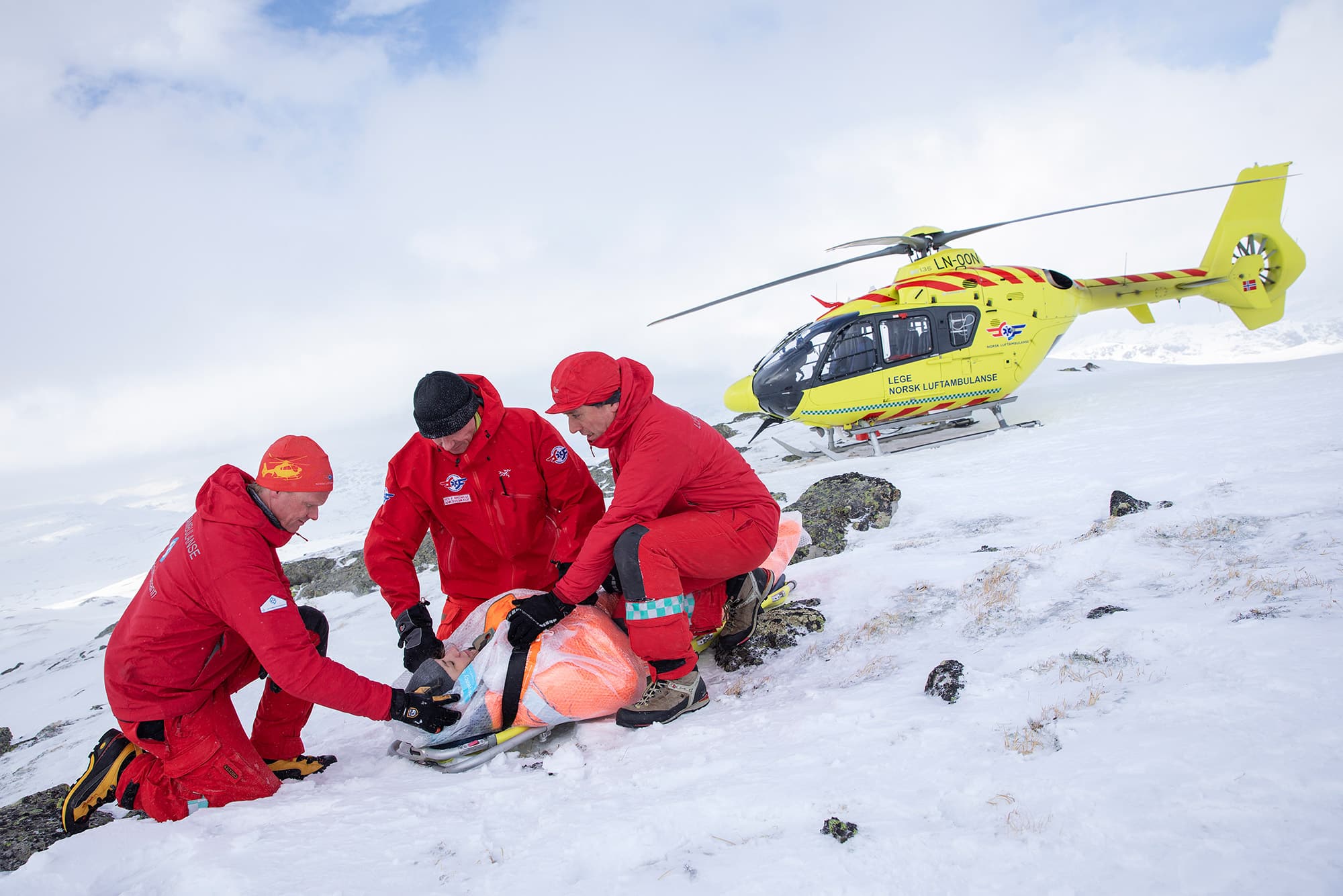Luftambulansecrew hjelper pasient under øvelse på snødekt fjelltopp.