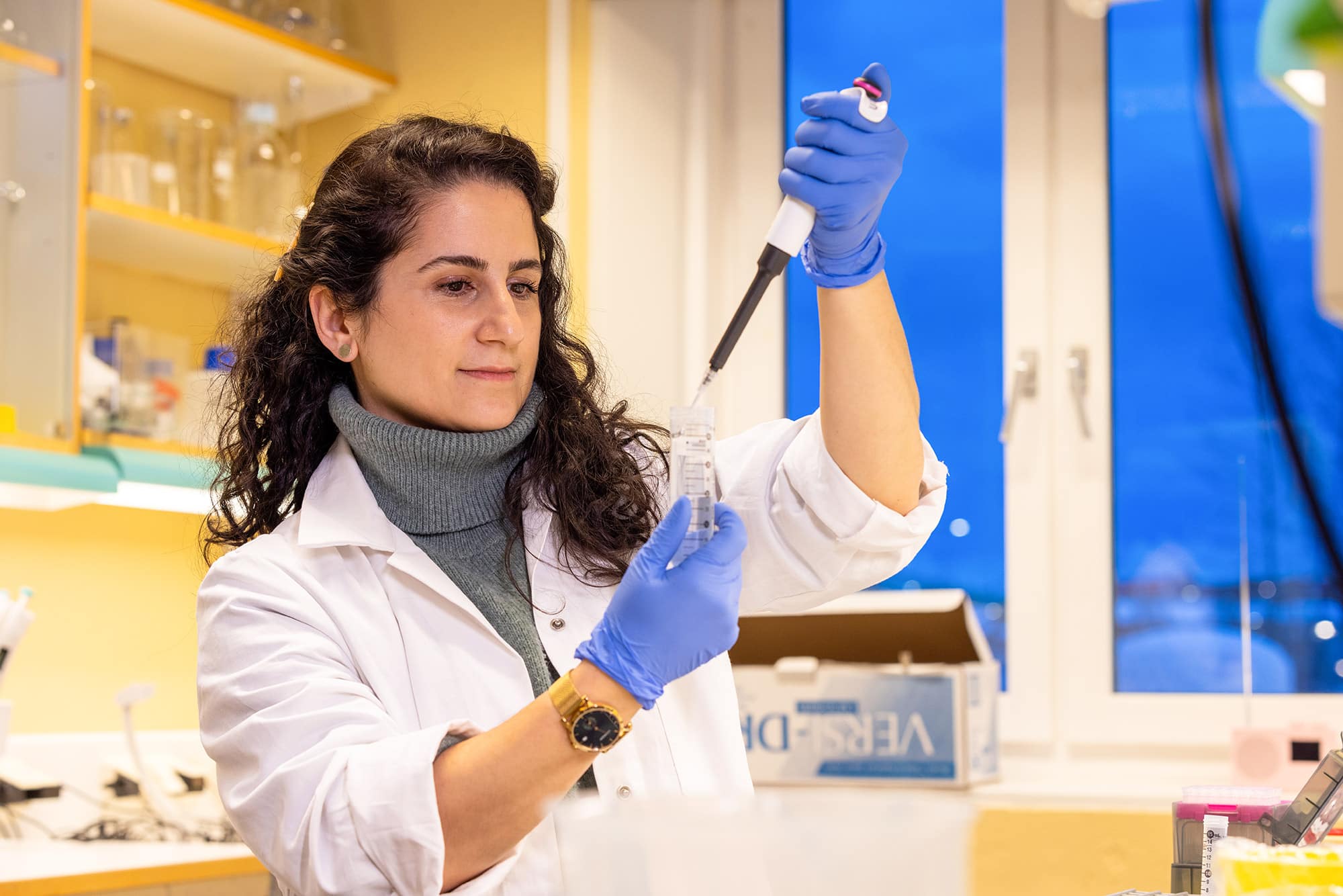 Forsker Adrina Kalasho Kuzmiszyn i labfrakk med glass og pipette på laboratoret.