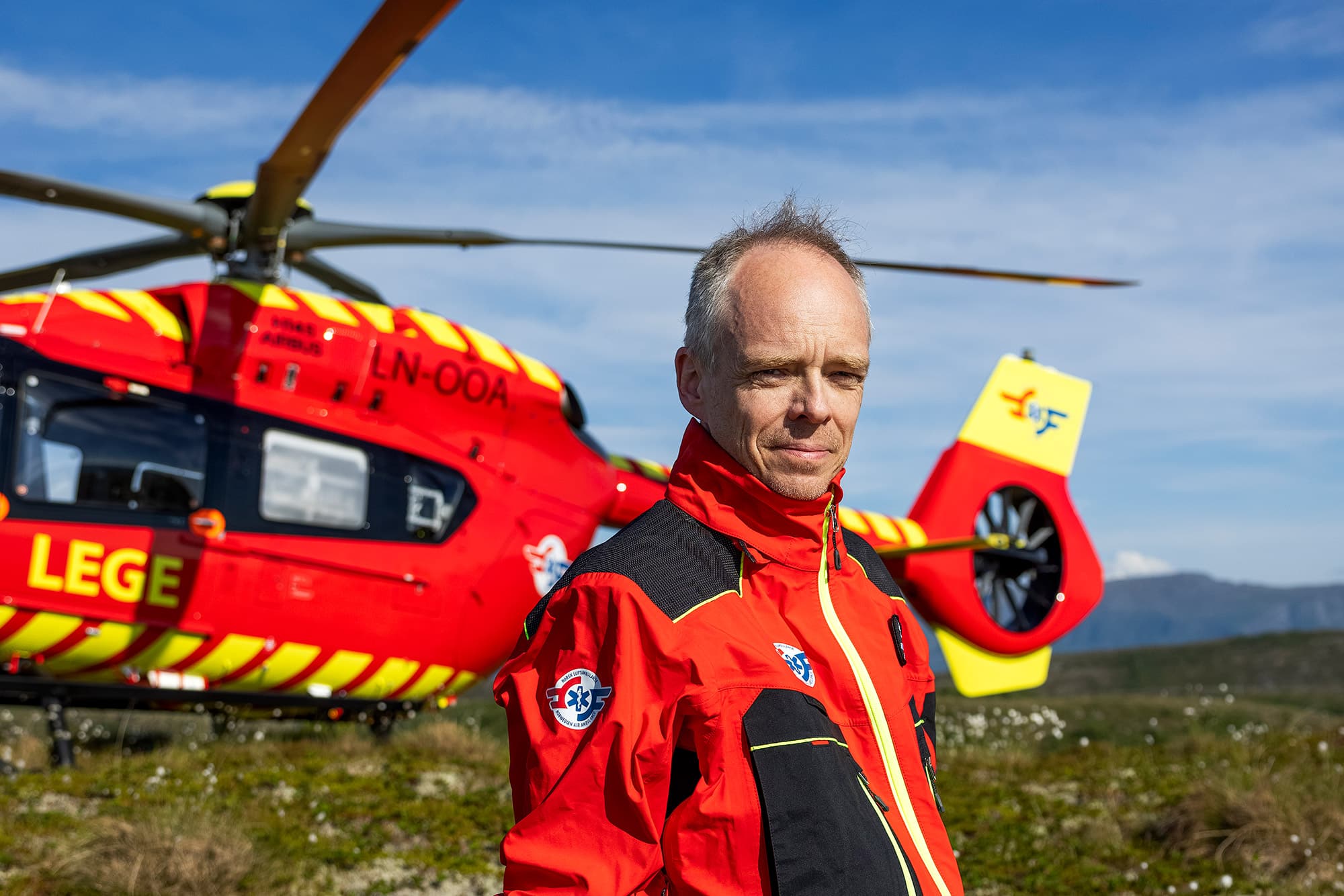 Sjeflege Stephen Sollid foran legehelikopteret, som har landet på en gresskledd slette.