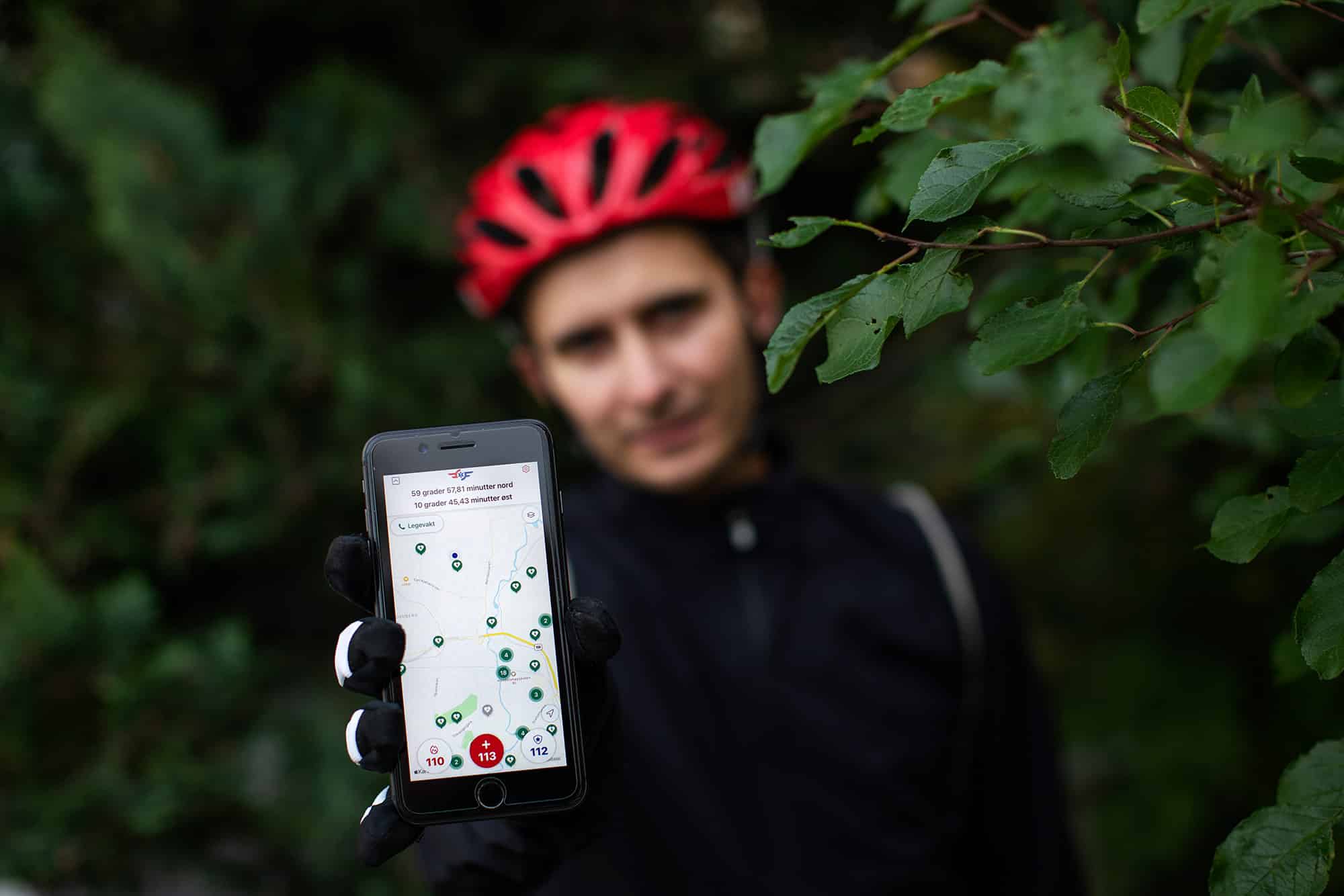 Mann med sykkelhjelm holder frem mobiltelefon med 113-appen aktiv
