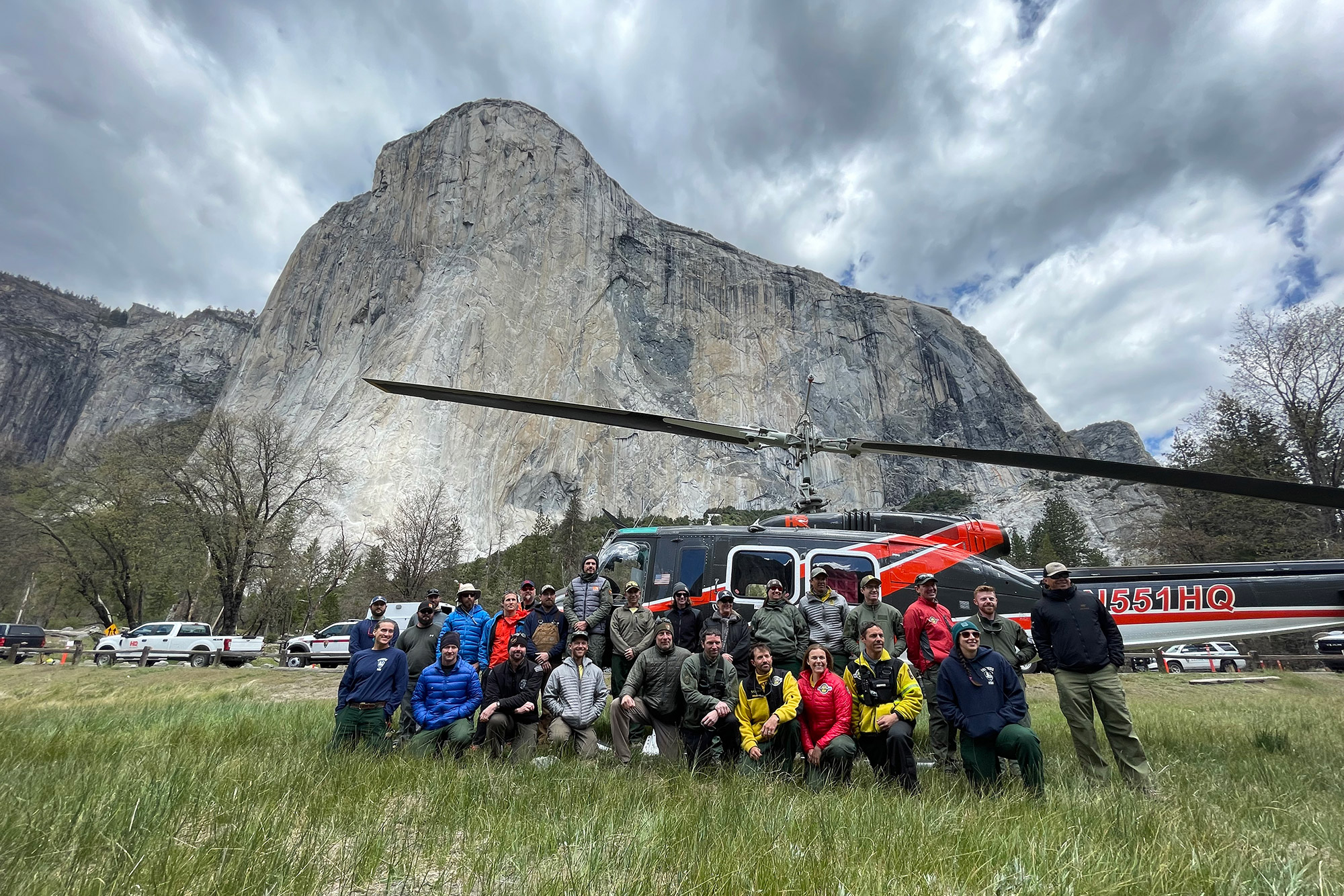 En stor gjeng redningsarbeidere sitter foran helikopteret, med Yosemite-fjell i bakgrunnen.