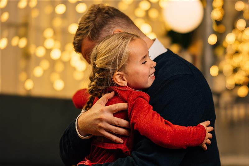 En fire år gammel datter som klemmer faren sin. Det er julelys i bakgrunn.