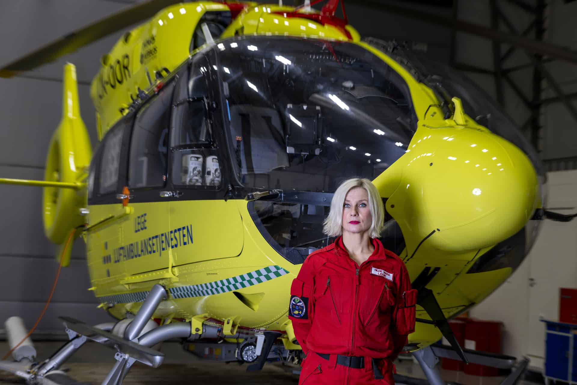 Portrett av Stiftelsen Norsk Luftambulanses nye sjeflege Hilde Wara foran et gult legehelikopter.
