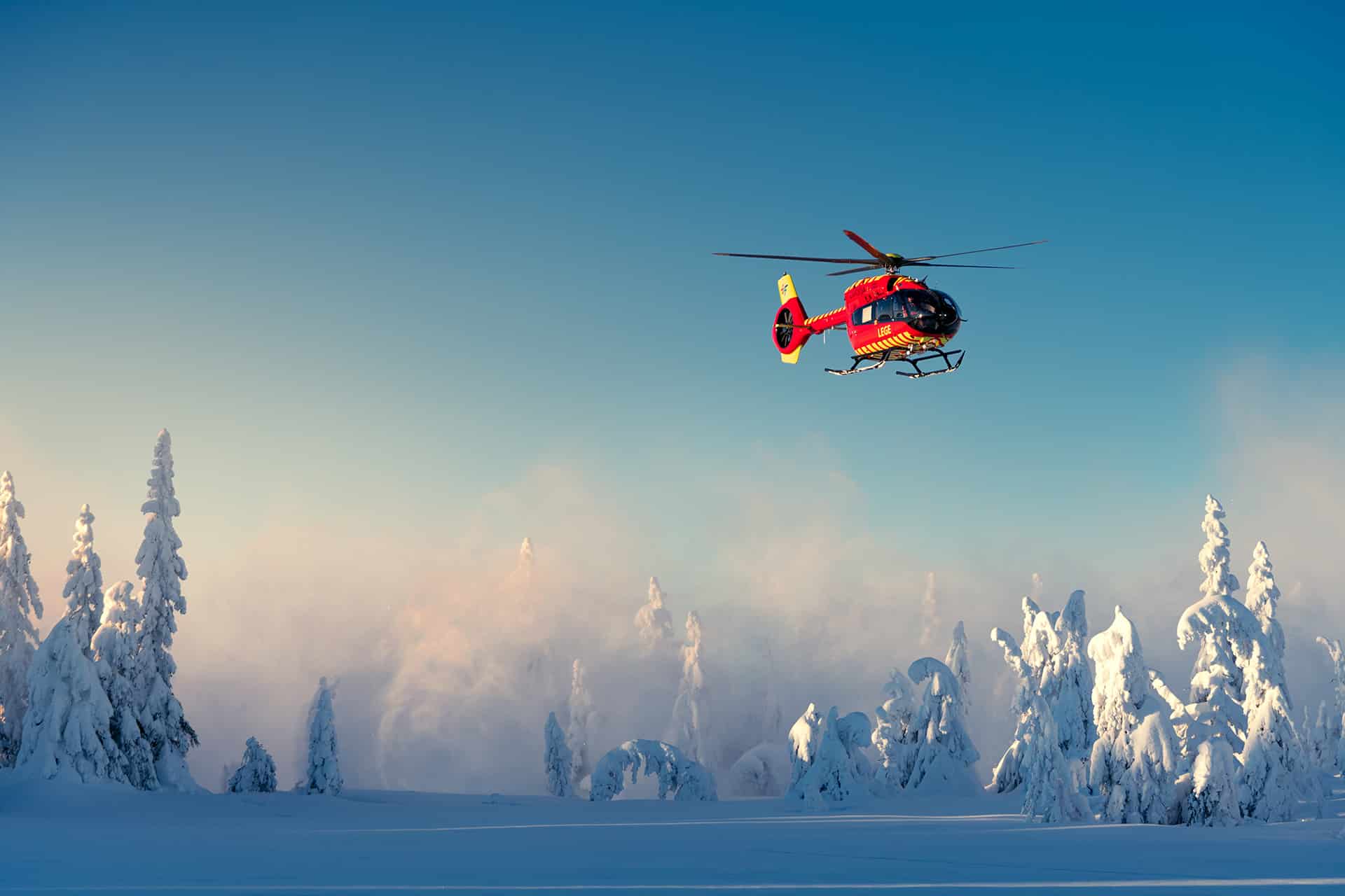 Rødt helikopter flyr over vinterlandskap