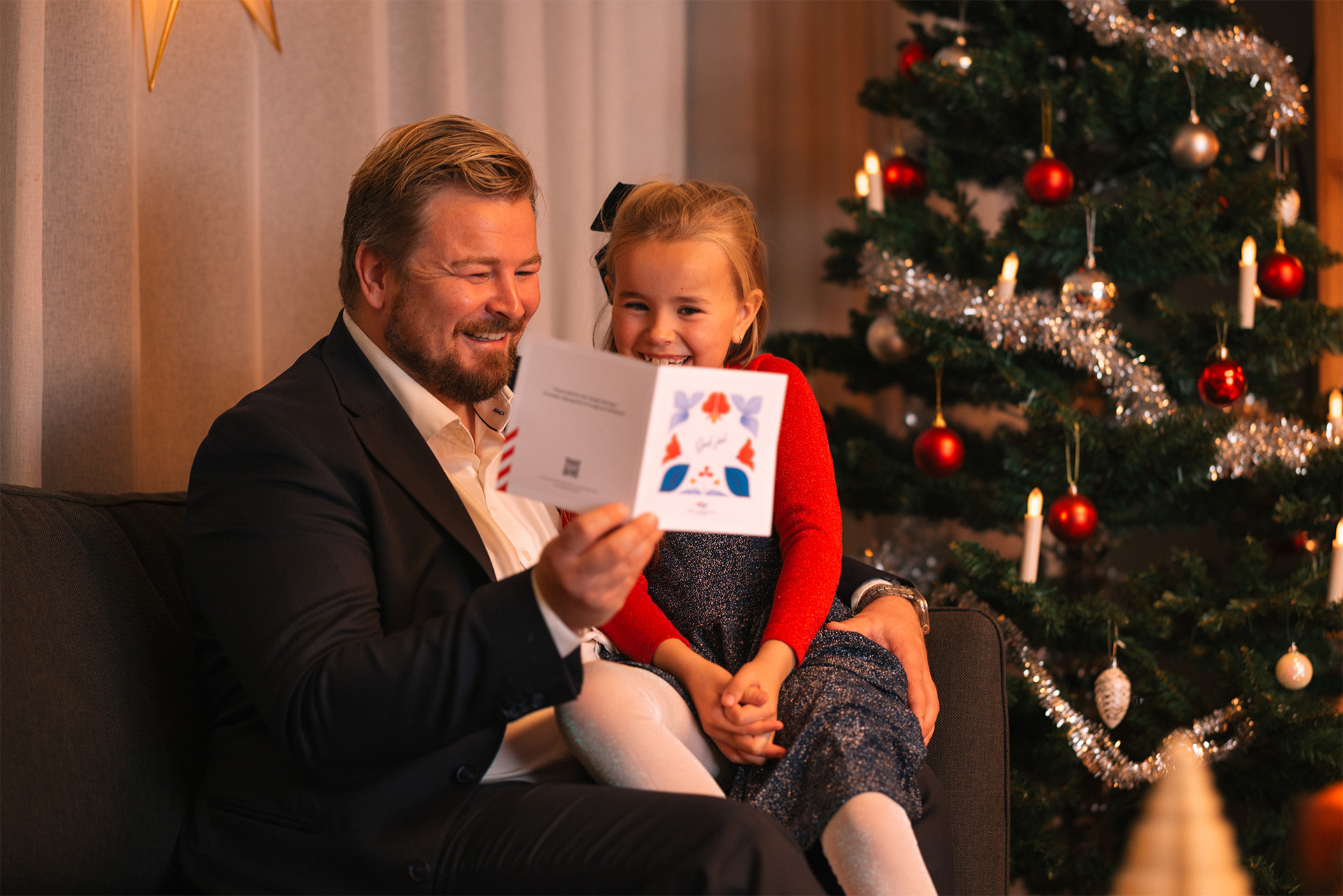 Far og datter sitter smilende i sofaen med et julegavekort.