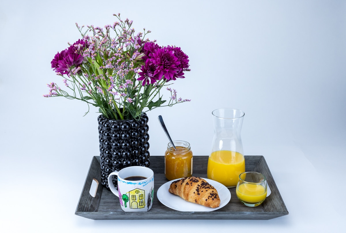 Frokostbrett med croissant, juice, kaffe og blomster til morsdagen. 