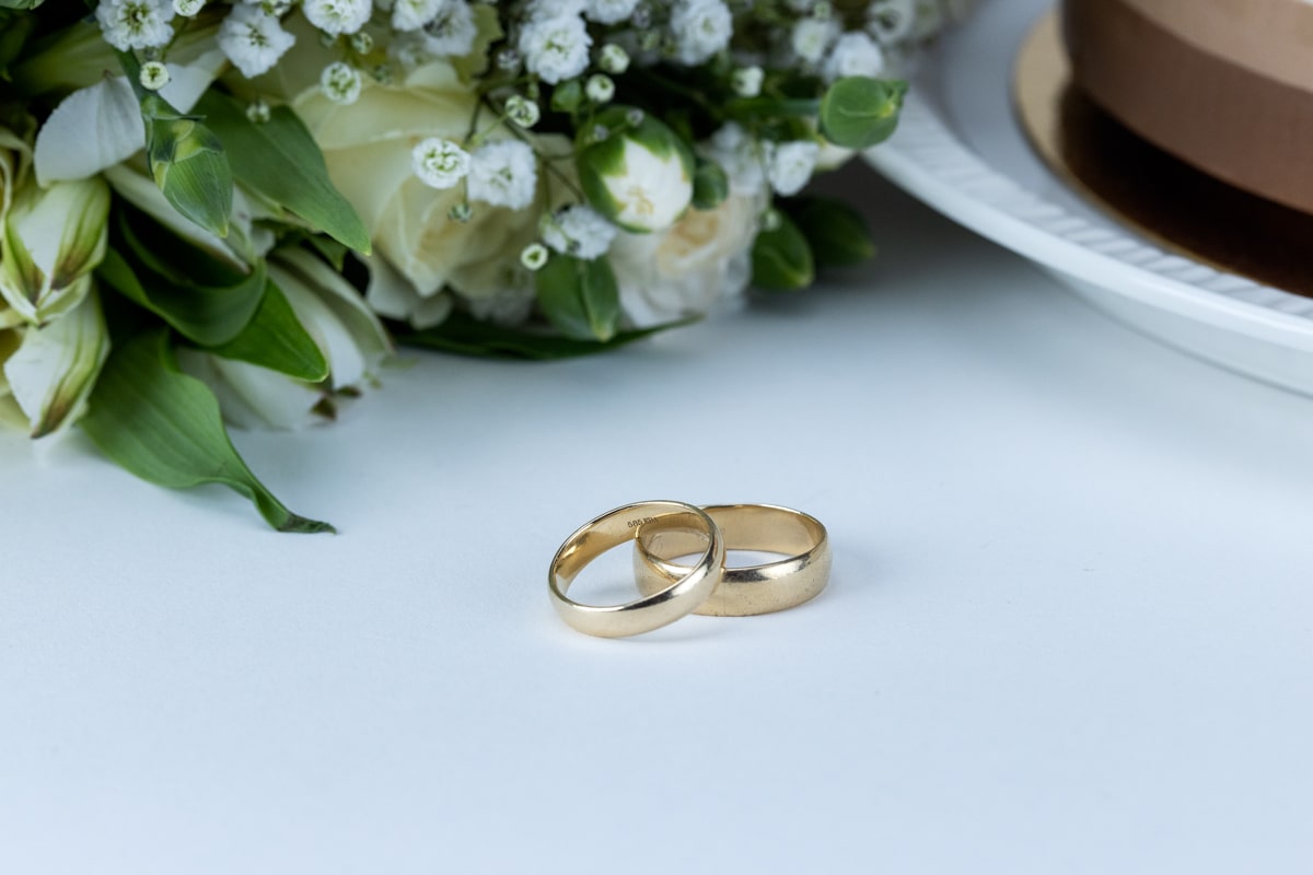 To gifteringer i gull som ligger på et bord med hvite blomster i bakgrunnen.