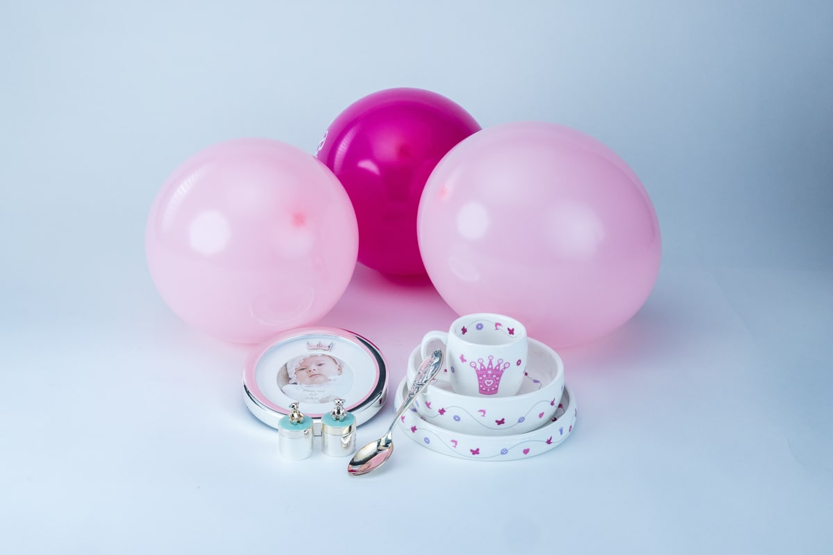 Dåpsgaver til jente på et bord med rosa dekorasjoner, blant annet sølvskje, sølvramme, tallerken og kopp.