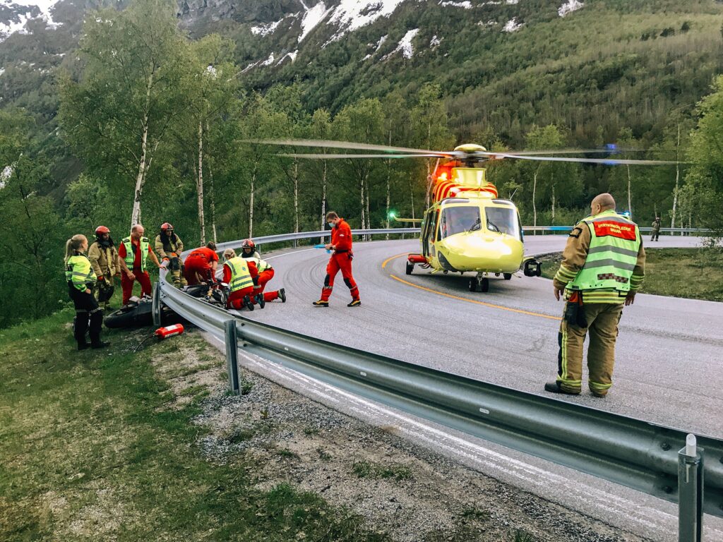 Bilde fra skadestedet da Valon Aliji krasjet inn i autovernet på motorsykkel. Avbildet er politi, ambulansepersonell, brann og helikoptercrew og et gult legehelikopter.