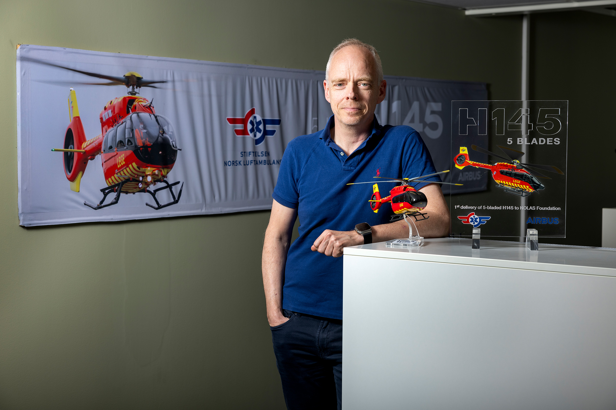 Generalsekretær Stephen J.M. Sollid på kontoret, med helikoptermodeller i forgrunnen og en banner med helikopter i bakgrunnen.