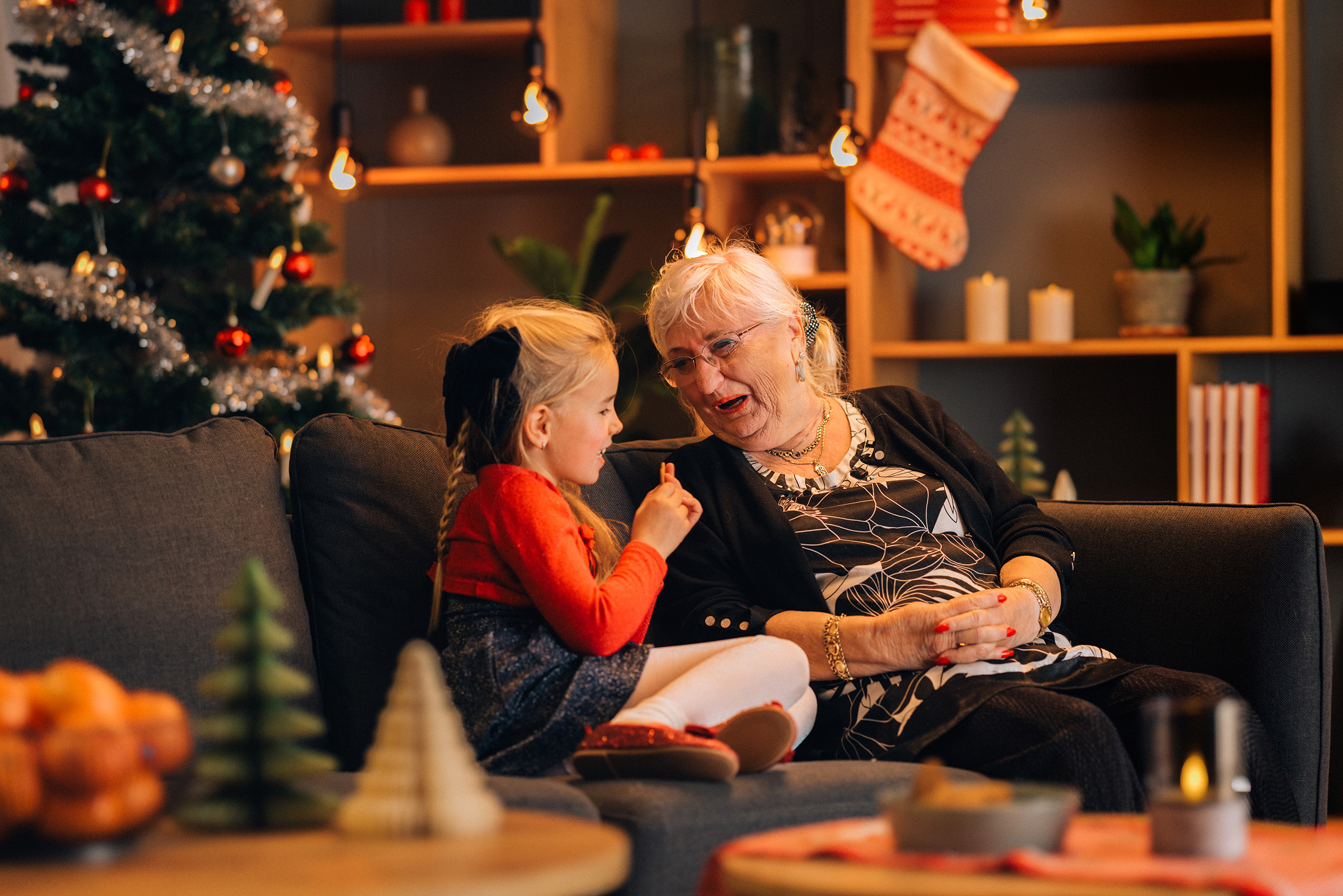 Jente og bestemor sitter på en sofa og ler. Det er pyntet til jul. 