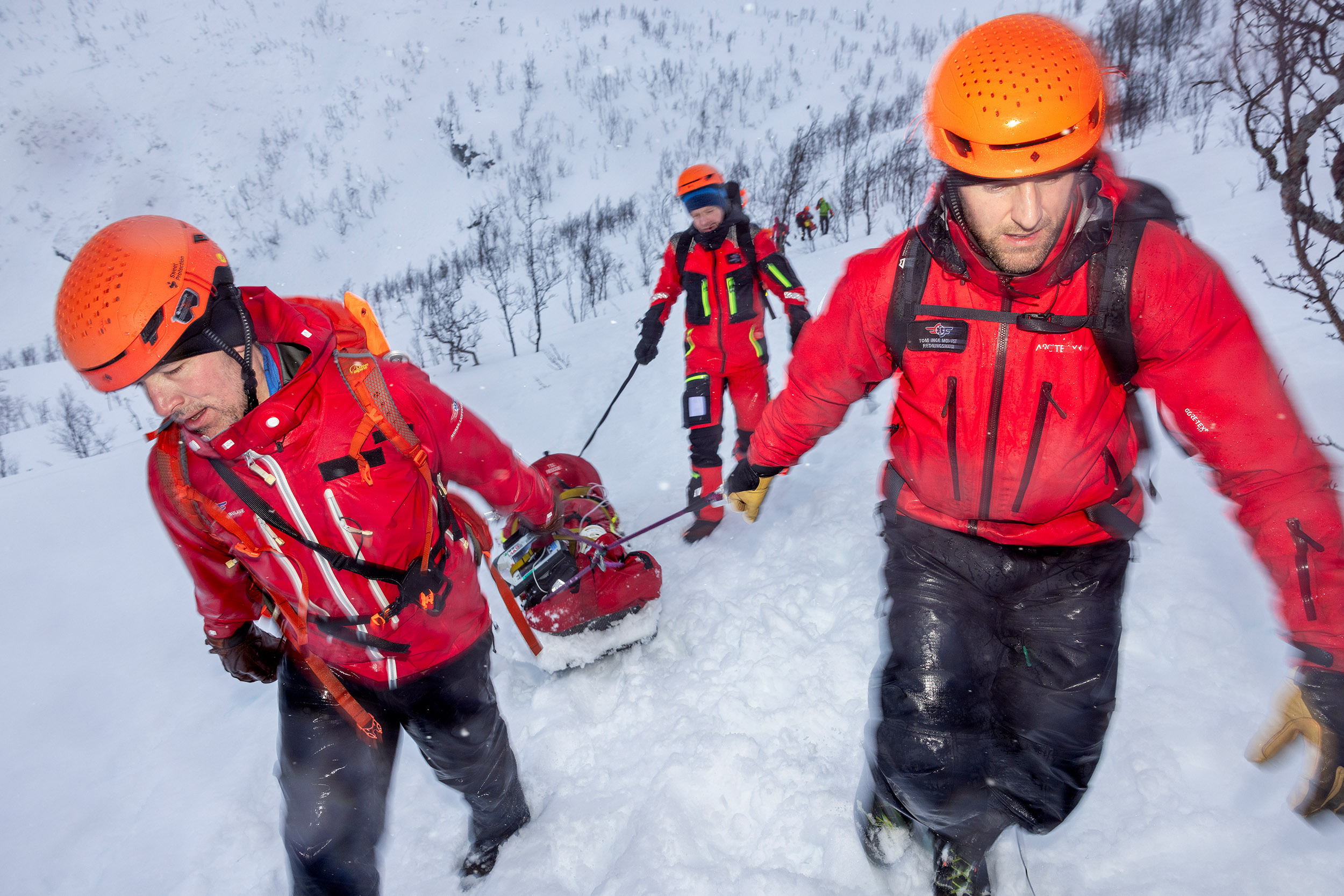 Helikoptercrew trener. HEMS Camp Tromsø 2025.en pulk fraktes opp til et skredoffer. Det er tungt arbeid å dra den opp gjennom snøen, i sludd og regn.