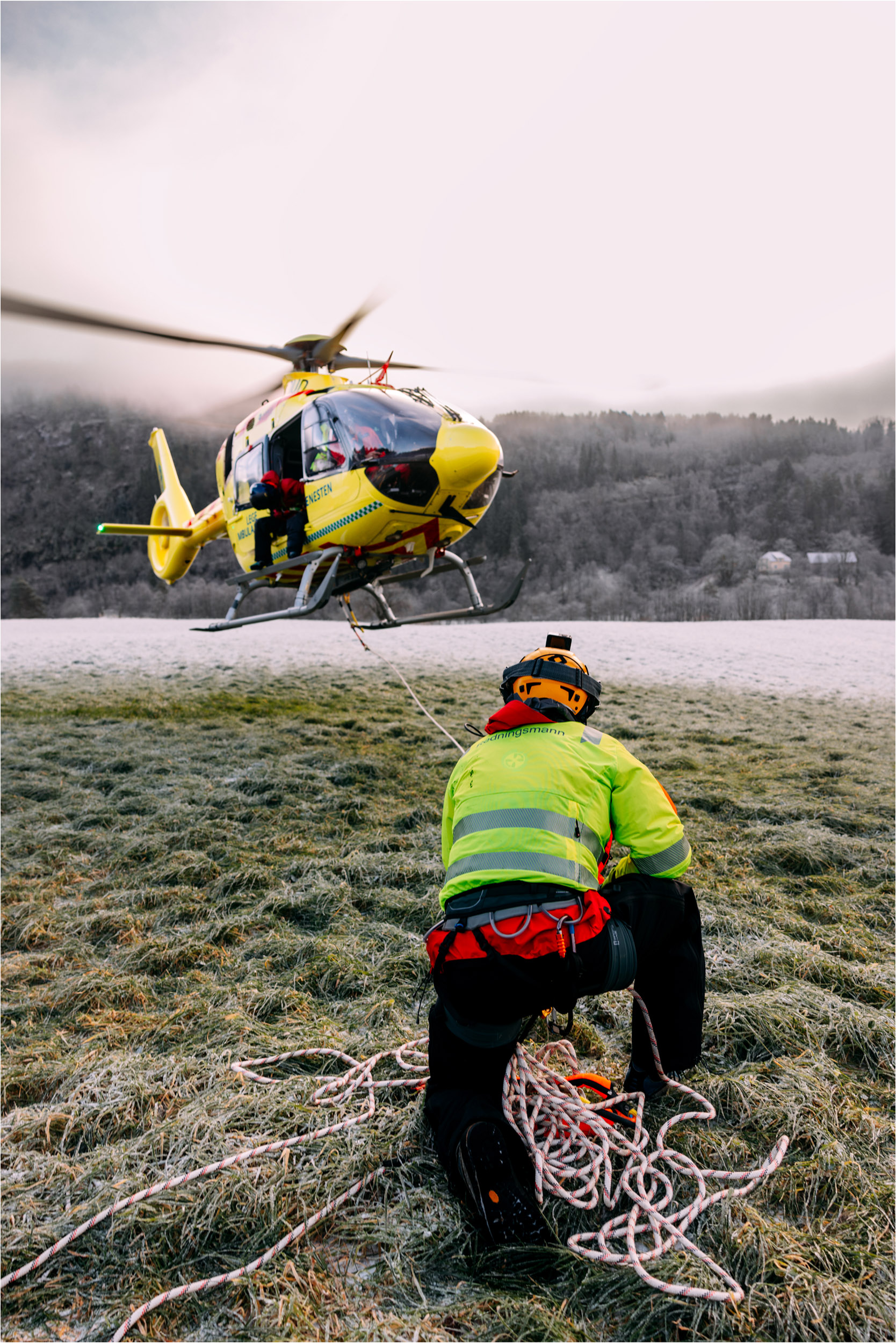 Gult legehelikopter er i ferd med å ta av. Redningsmann Anders Kroken har festet seg til helikopteret med tau for å trene på underhengende redning ved helikopterbasen i Førde.