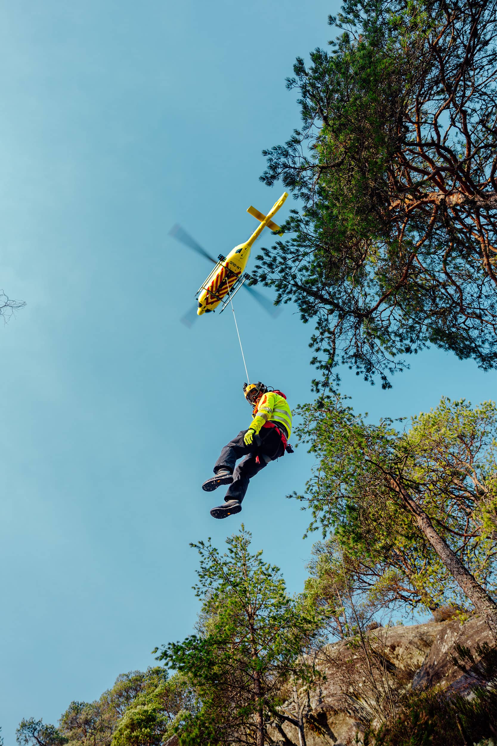 Redningsmann Anders Kroken hengende i tau under helikopteret. Crewet trener på underhengende redning i Førde.