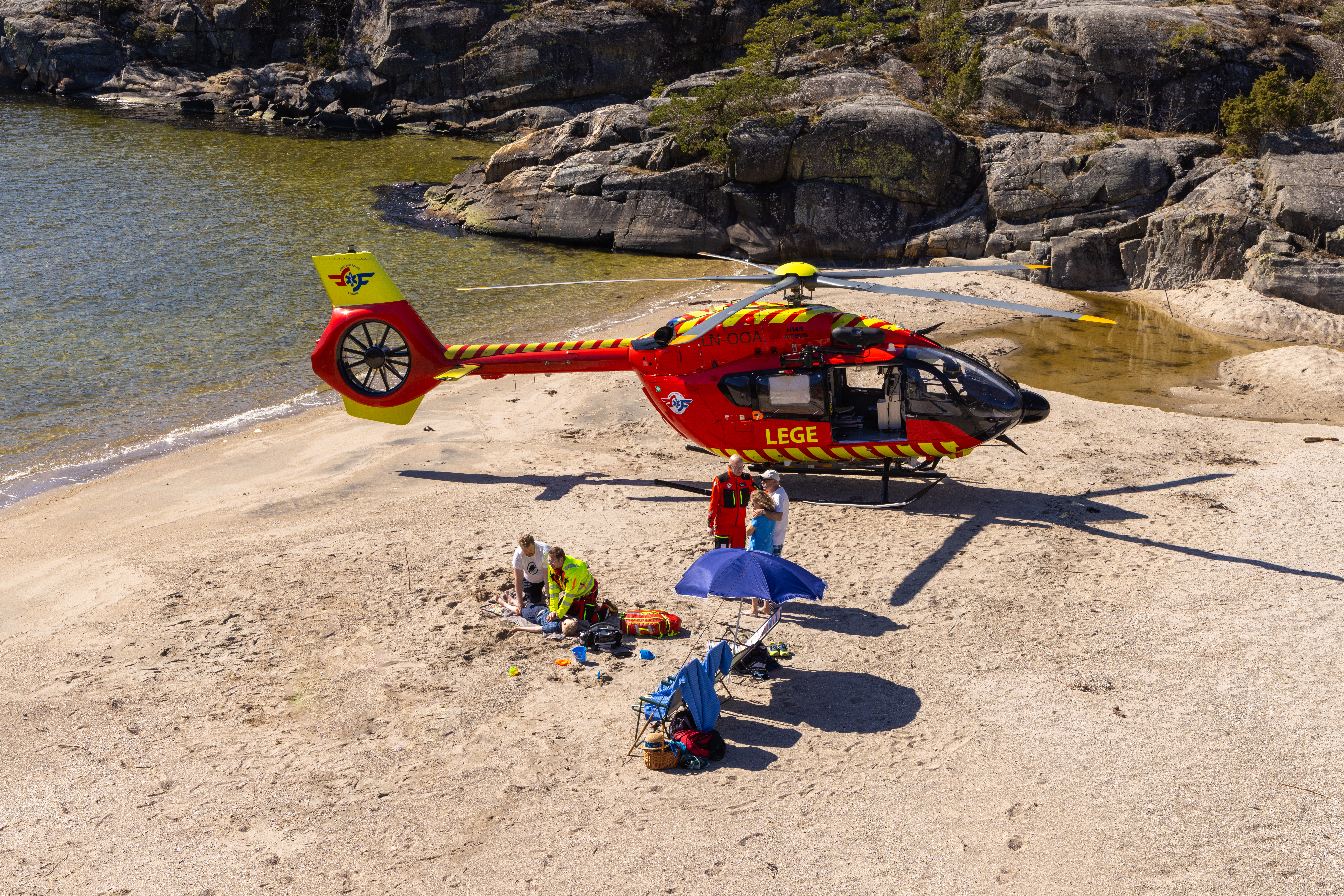 En akutt situasjon på en strand med hvor helikopter og helsepersonell har landet. 