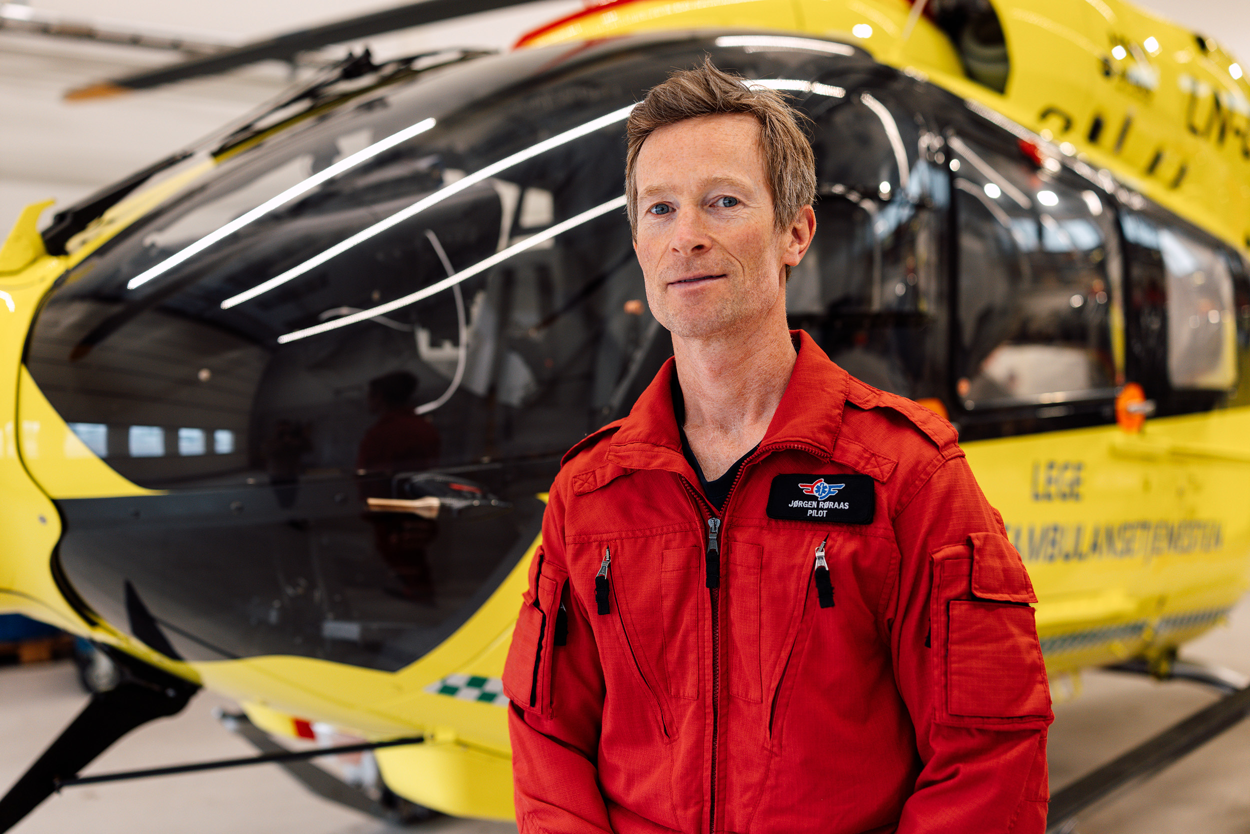 Portrett av pilot Jørgen Røraas foran gult helikopter
