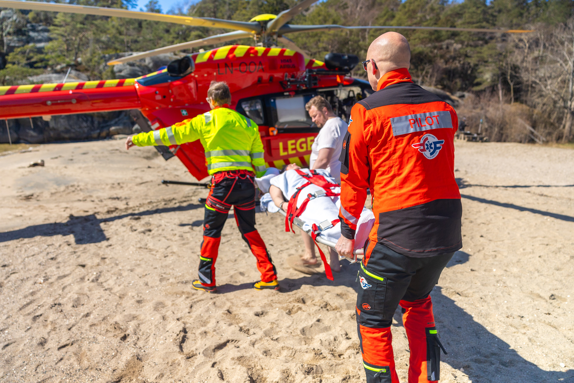 Luftambulanselege, pilot og pårørende bærer pasient mot helikopteret.