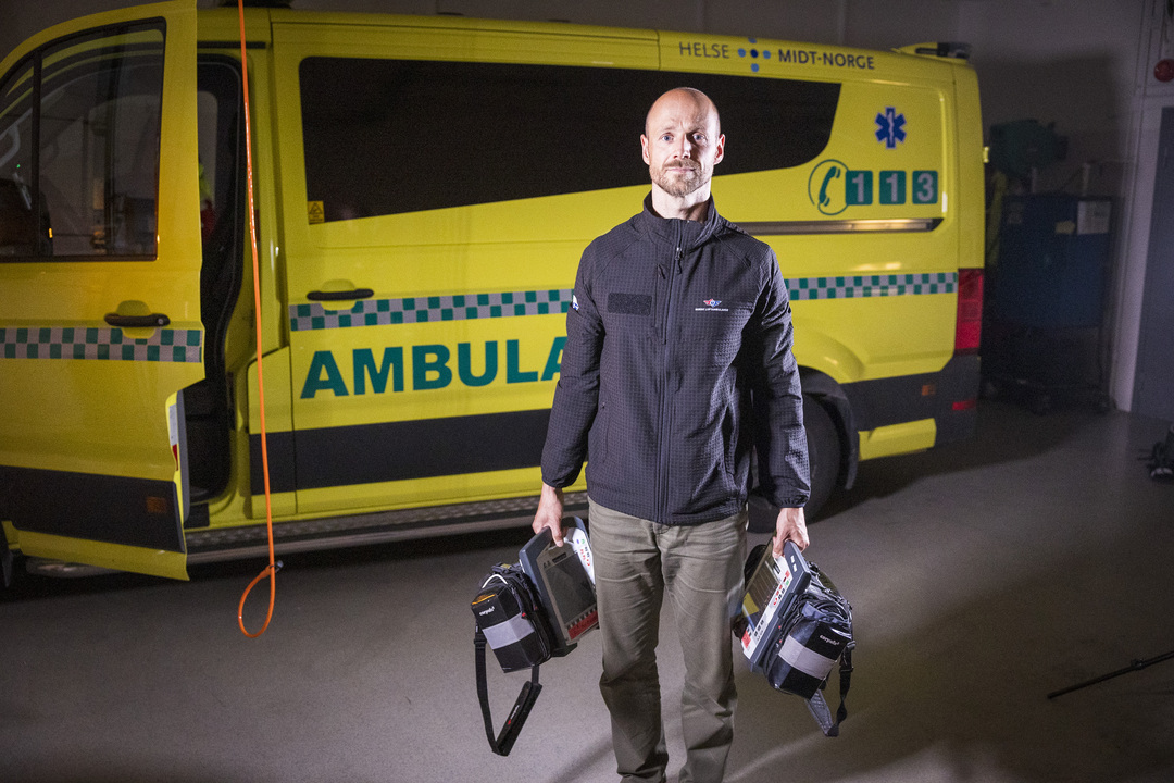 Researcher holding two defibrillators in front of an ambulance 