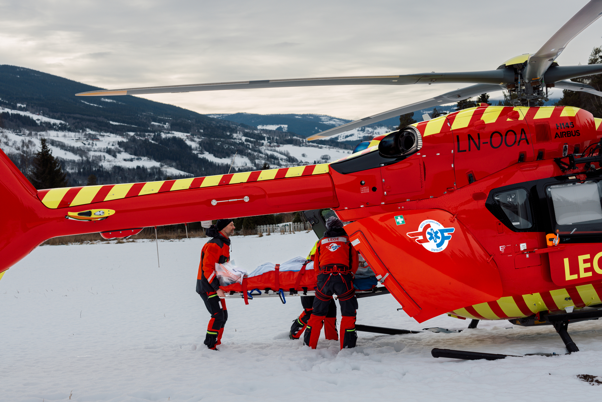 Crew bærer pasient på båre inn i helikopteret